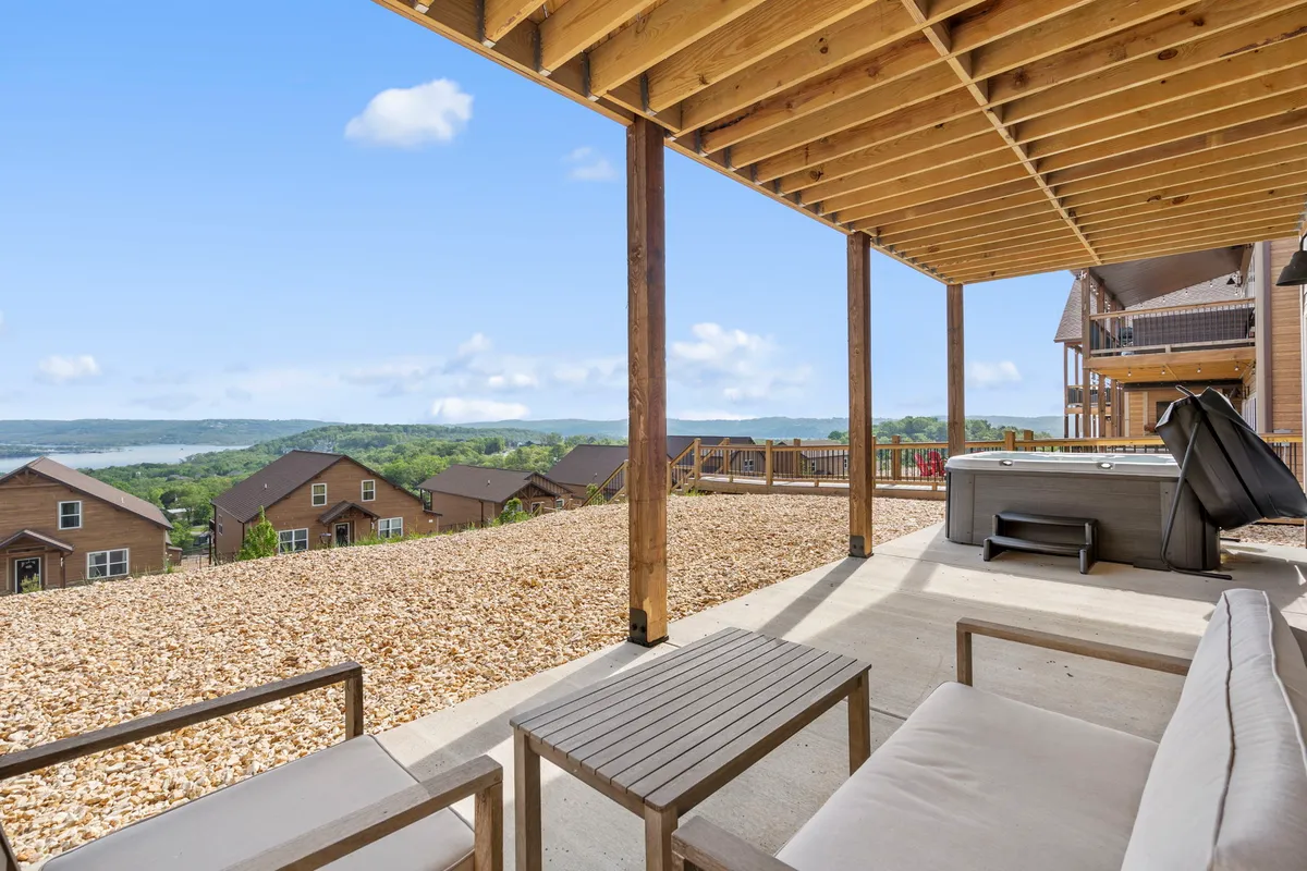 An inviting outdoor hot tub sits on a spacious deck, surrounded by comfortable seating and set against a backdrop of rolling hills and open sky. The landscape beyond the deck hints at tranquil mornings or starlit evenings spent soaking and socializing outdoors.