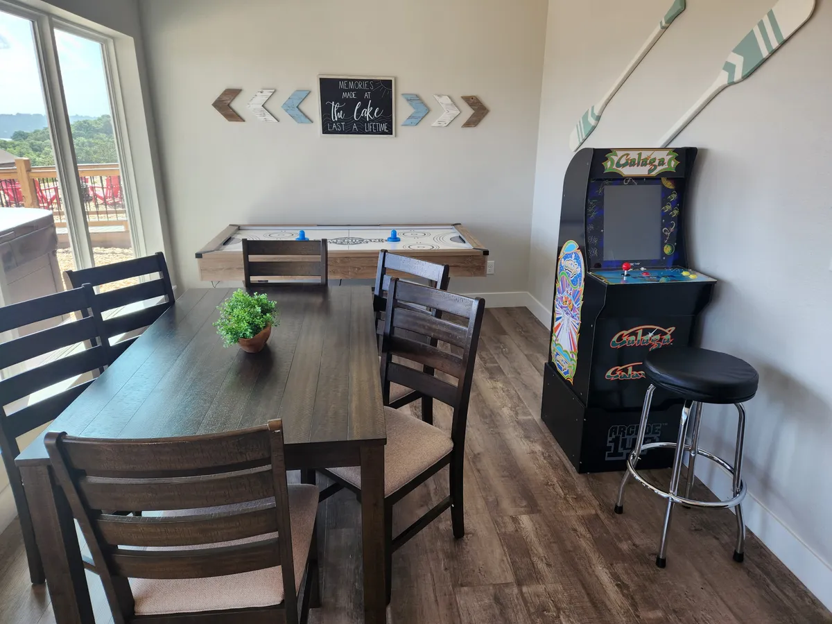 This image captures a vibrant game area featuring a dining table, an air hockey table, and an arcade game. The atmosphere is fun and relaxed, inviting guests to enjoy friendly competition and shared meals in a lively setting.