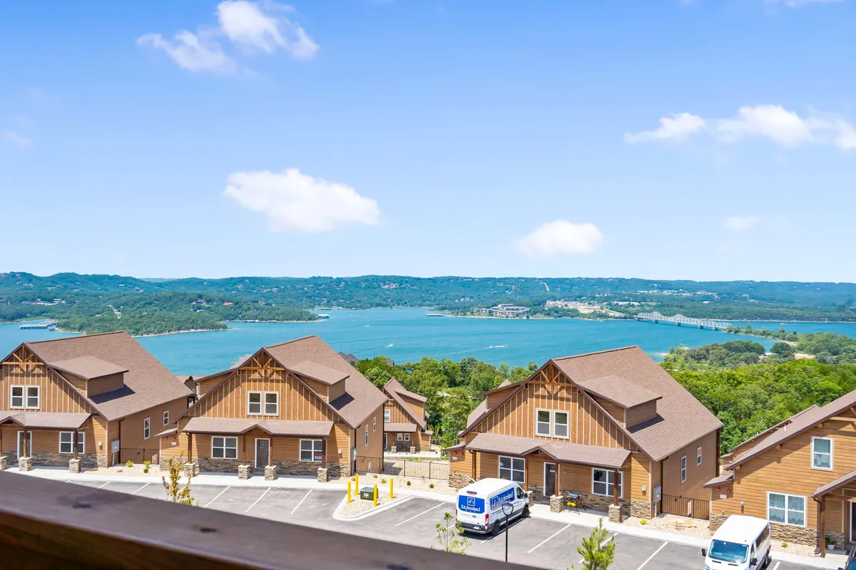 A tranquil lake stretches out before a handful of rustic wooden cabins nestled among green hills. The golden light of sunset bathes the water and cabins, creating a peaceful lakeside atmosphere ideal for family gatherings or quiet reflection.