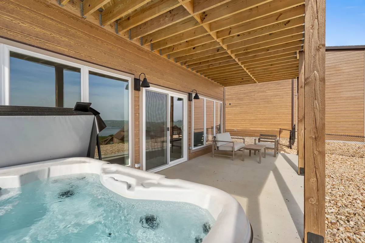 A stylish exterior view featuring a private hot tub and inviting outdoor seating area, framed by large windows that hint at the comfort within. The sky glows with sunset colors, and the setup suggests a perfect spot to unwind while enjoying the surrounding views.