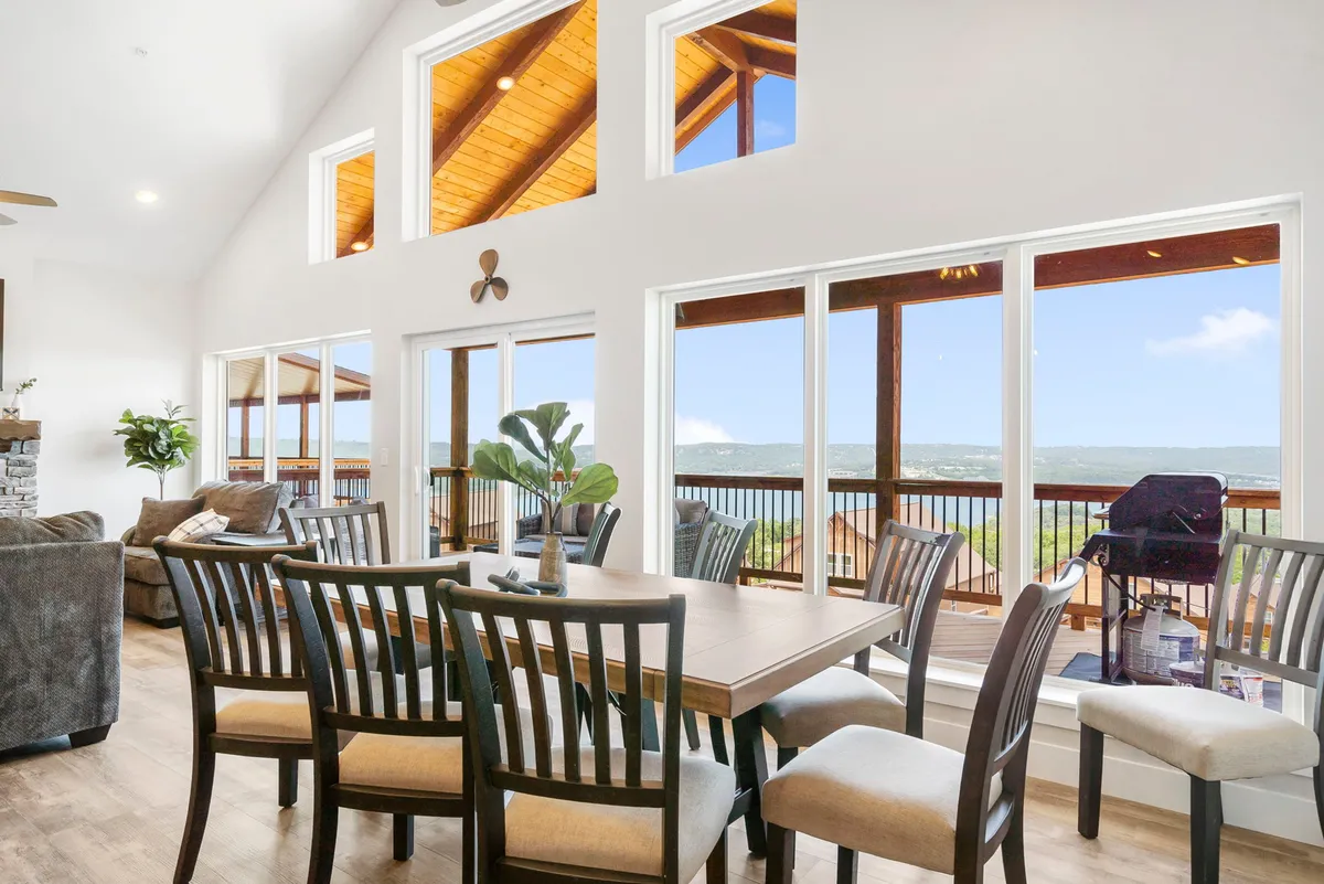 The image showcases a spacious interior with a warm, inviting dining area set beneath a striking wooden ceiling. Large windows frame gorgeous lake views, filling the room with natural light. Plush, comfortable seating invites guests to relax and gather together, making it the perfect setting for family meals or friendly get-togethers.