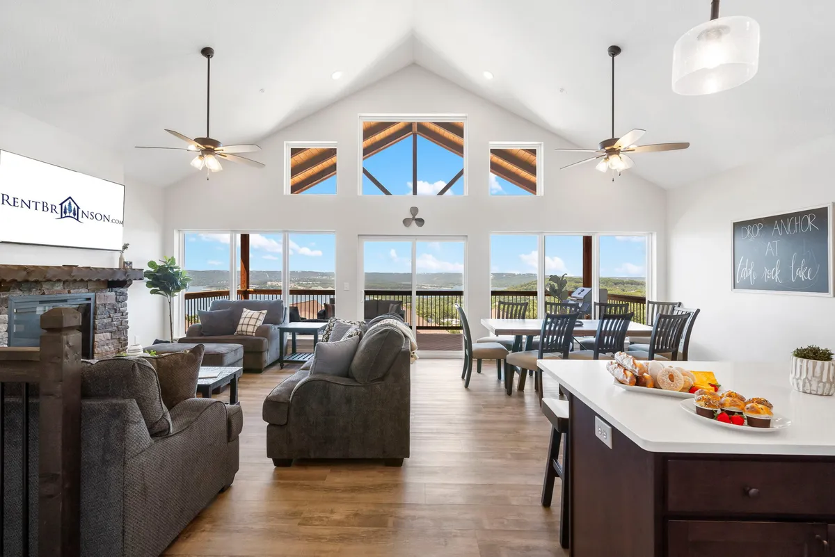 A bright, open-concept communal space featuring large windows with views, a comfortable seating area, a spacious dining table, and a kitchen island adorned with fresh pastries. The room is filled with natural light and offers plenty of space for groups to gather, dine, and socialize.