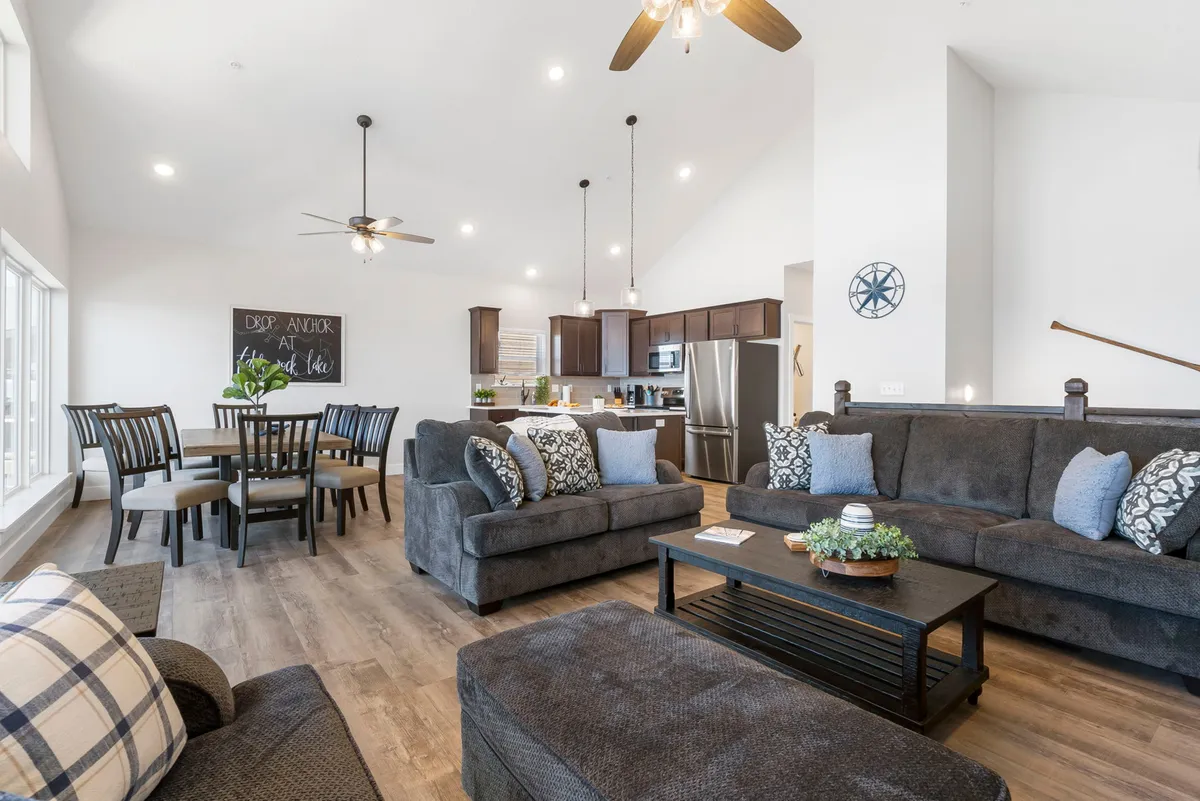 A welcoming open-plan living and dining area with plush sofas decorated with pillows, a dining table set for a meal, and a kitchen area in the background. The ambiance is warm and inviting, ideal for relaxation and group gatherings.