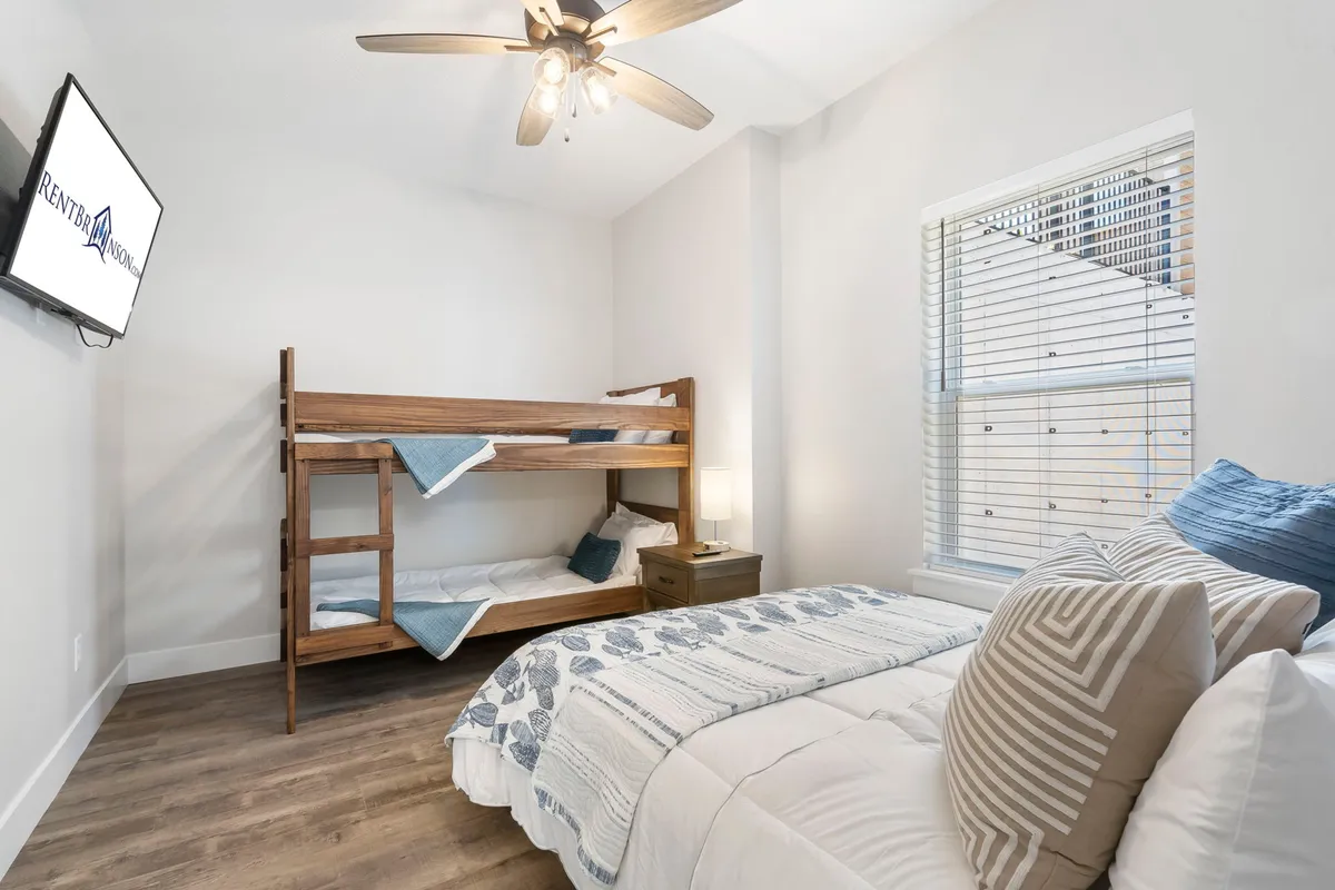 A spacious family-friendly suite showcasing a bunk bed beside a queen/king bed, with cheerful decorative pillows and a mounted television. The arrangement is ideal for families, allowing children to sleep close to parents in a relaxing setting.