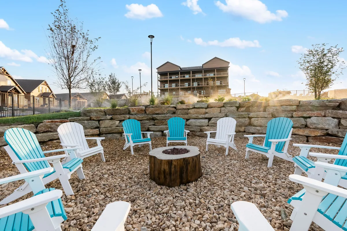 A cozy exterior scene showcases a communal fire pit surrounded by Adirondack chairs, with a building in the background. The warm glow of the fire creates a welcoming space for guests to gather, socialize, and share stories as evening falls.
