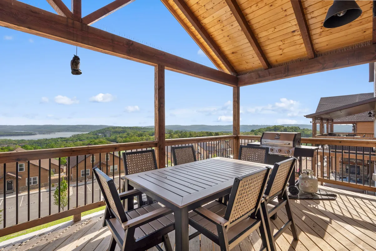 A spacious outdoor dining area features a sturdy wooden table, black chairs, and a grill set against a backdrop of scenic lake views. The setup is ideal for hosting gatherings or barbecue parties, with open sky and tranquil water creating a lively yet relaxed atmosphere.