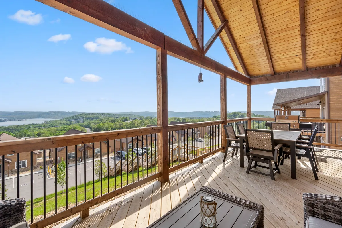 A serene wooden deck with a dining table and chairs, bordered by a railing and a hanging lantern, overlooking scenic hills and water. The atmosphere is peaceful and ideal for both morning coffee and evening gatherings, capturing the panoramic lake views described.