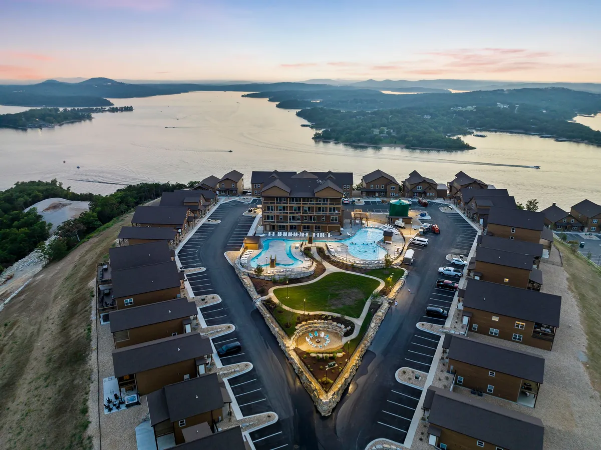 A beautifully landscaped resort area featuring two sparkling swimming pools, lush gardens, and a serene waterfront view. Residential buildings line the background, showing the resort’s blend of privacy and community amenities. Lounge chairs and greenery add a luxurious, relaxing ambiance.