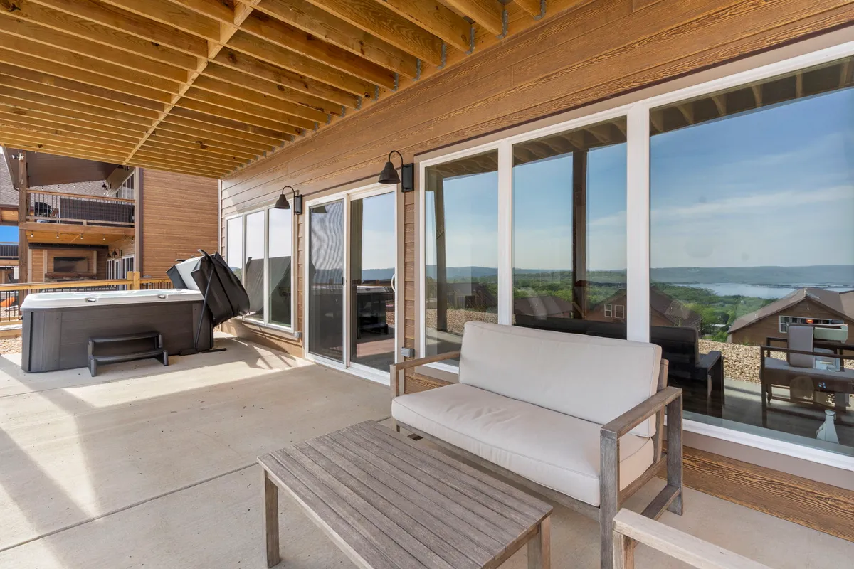 A tranquil outdoor area featuring a hot tub and cozy seating, set before expansive windows with views of the surrounding landscape. The patio-style setting is perfect for unwinding after a day out, with space for both people and pets to relax.