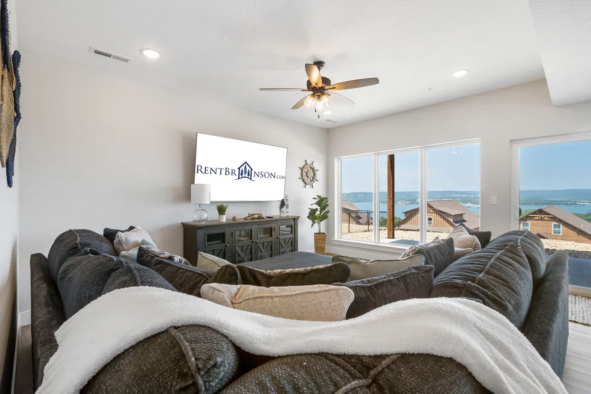 A spacious lounge area with a large sectional sofa, a TV, window views, a decorative wall clock, and indoor plants. The mood is cozy and welcoming, perfect for unwinding after a day of activities.